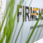 Firmenschild „FIRMENSITZ“ hinter Pflanzen als Symbol für eine professionelle Domiziladresse.